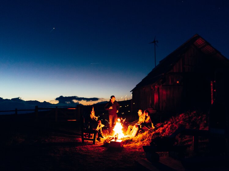 Gruppe sitzt rund ums Lagerfeuer und genießt die Abendstimmung auf der Alm | © Urlaub am Bauernhof Kärnten/ Daniel Gollner 