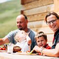 Familie sitzt auf der Bank for der Almhütte und jausnet in Kärnten  | © Urlaub am Bauernhof Kärnten / Daniel Gollner