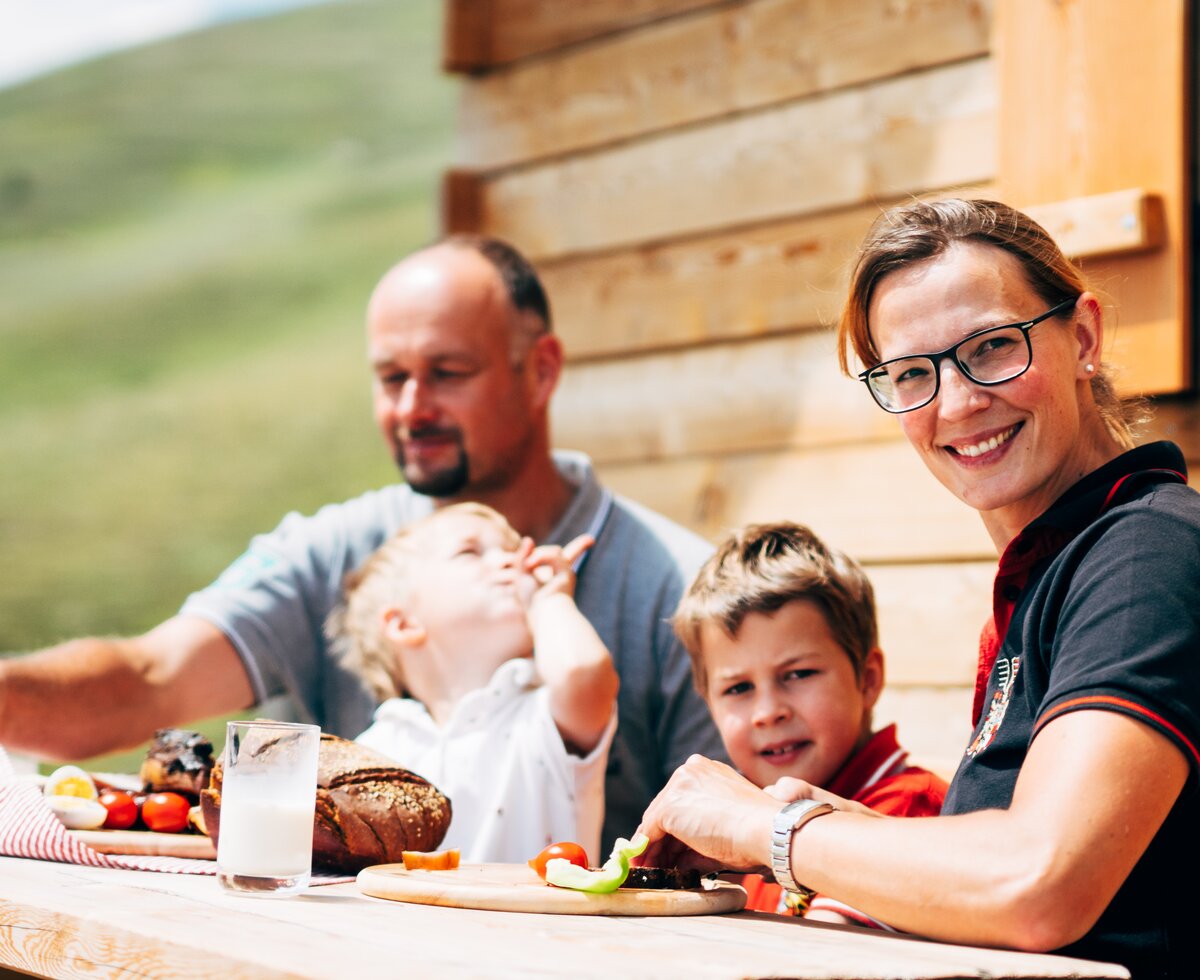 Familie sitzt auf der Bank for der Almhütte und jausnet in Kärnten  | © Urlaub am Bauernhof Kärnten / Daniel Gollner