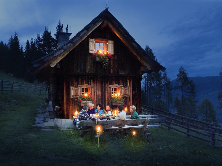 Gruppe sitzt in gemeinsamer Runde vor einer Almhütte und genießt den herbstlichen Abend | © Urlaub am Bauernhof Kärnten/ Ernst P. Prokop