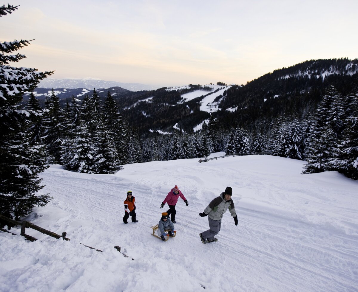 Familie spaziert mit Rodel auf der Alm in der verschneiten Winterlandschaft  | © Urlaub am Bauernhof/ Tom Lamm