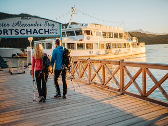 zwei Wanderer gehen am Steg zum Schiff in der Abenddämmerung | © Martin Hofmann / Wörthersee Tourismus GmbH