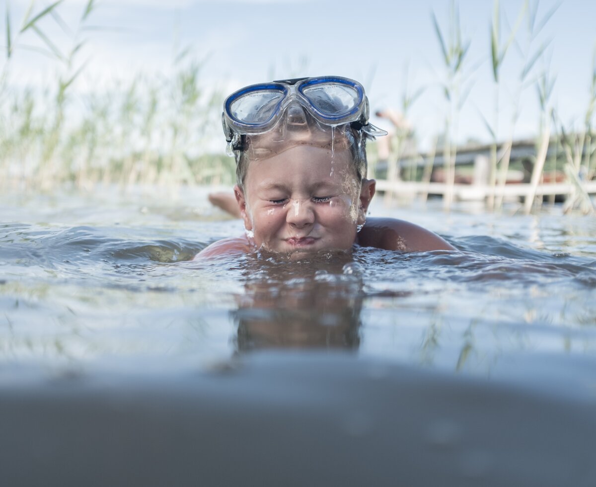 Bub mit Taucherbrille badet im See und prustet ins Wasser | © Urlaub am Bauernhof Oberösterreich / Robert Maybach