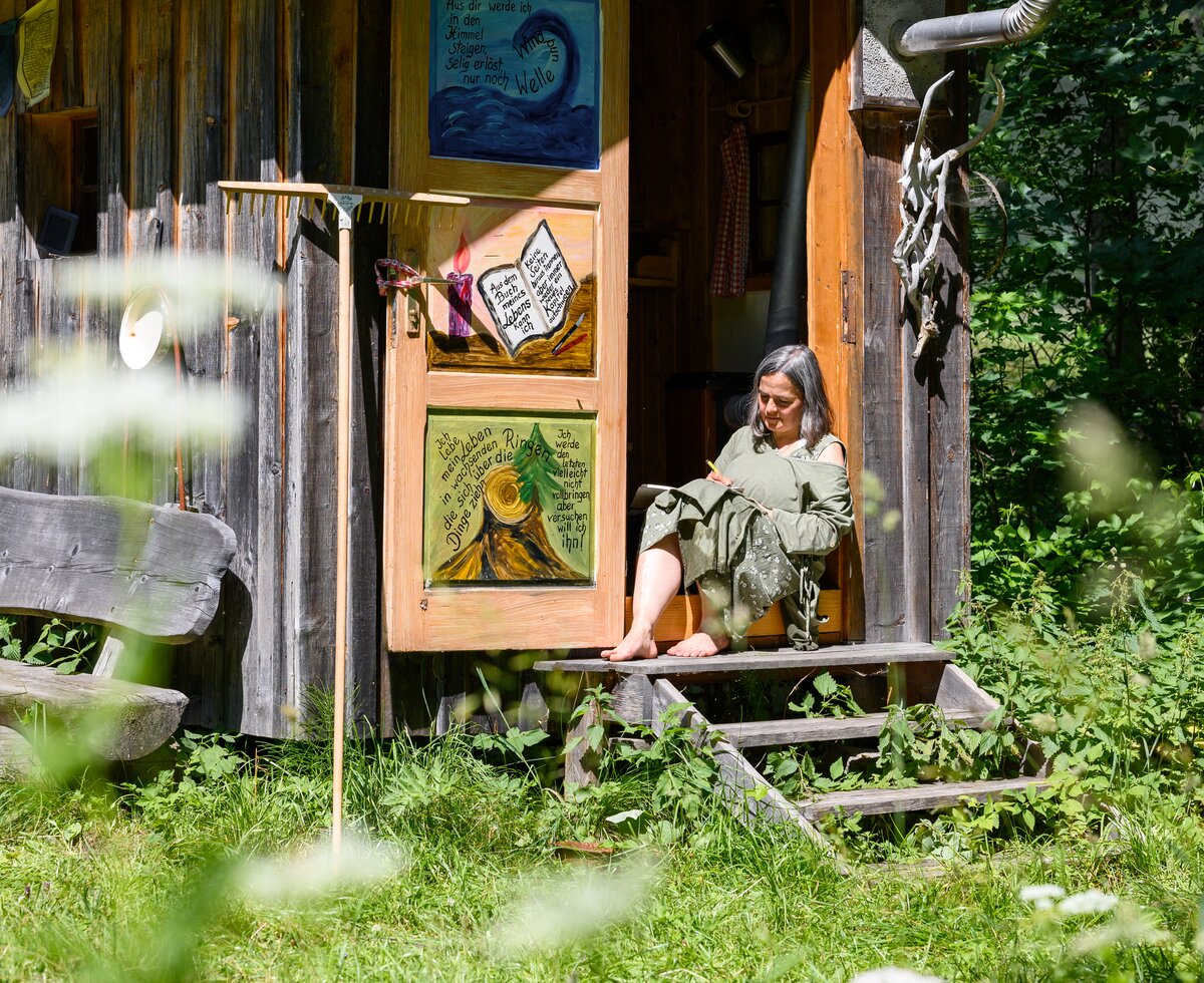 Frau sitzt auf Stufen vor einer Hütte | © Urlaub am Bauernhof