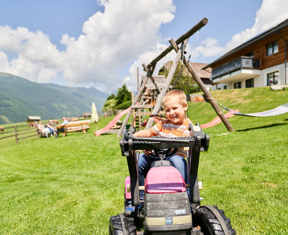 Bub fährt mit einem Spielzeugtraktor auf dem Spielplatz | © Urlaub am Bauernhof / Punkt und Komma