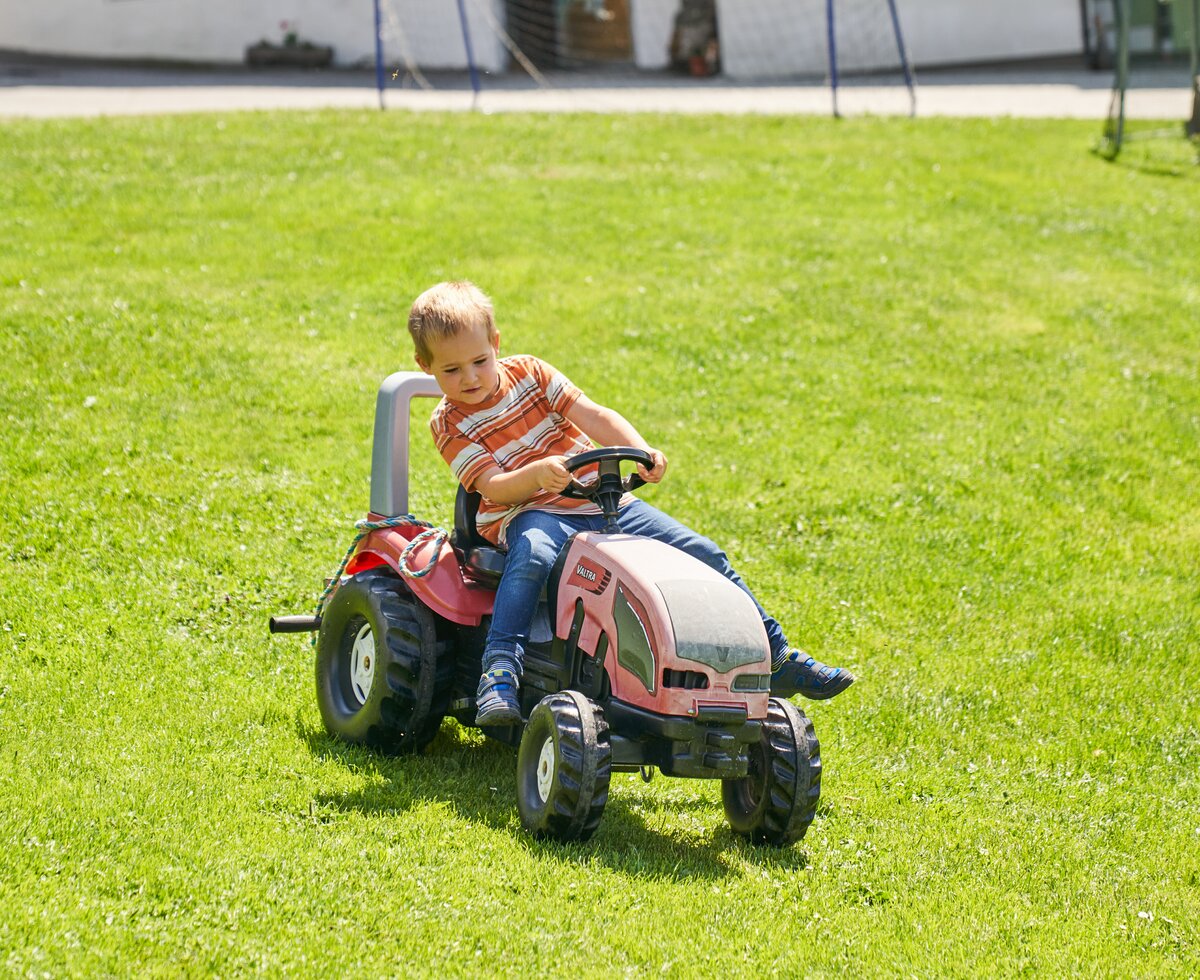 Bub fährt mit einem Spielzeugtraktor auf der Wiese | © Urlaub am Bauernhof / Punkt und Komma