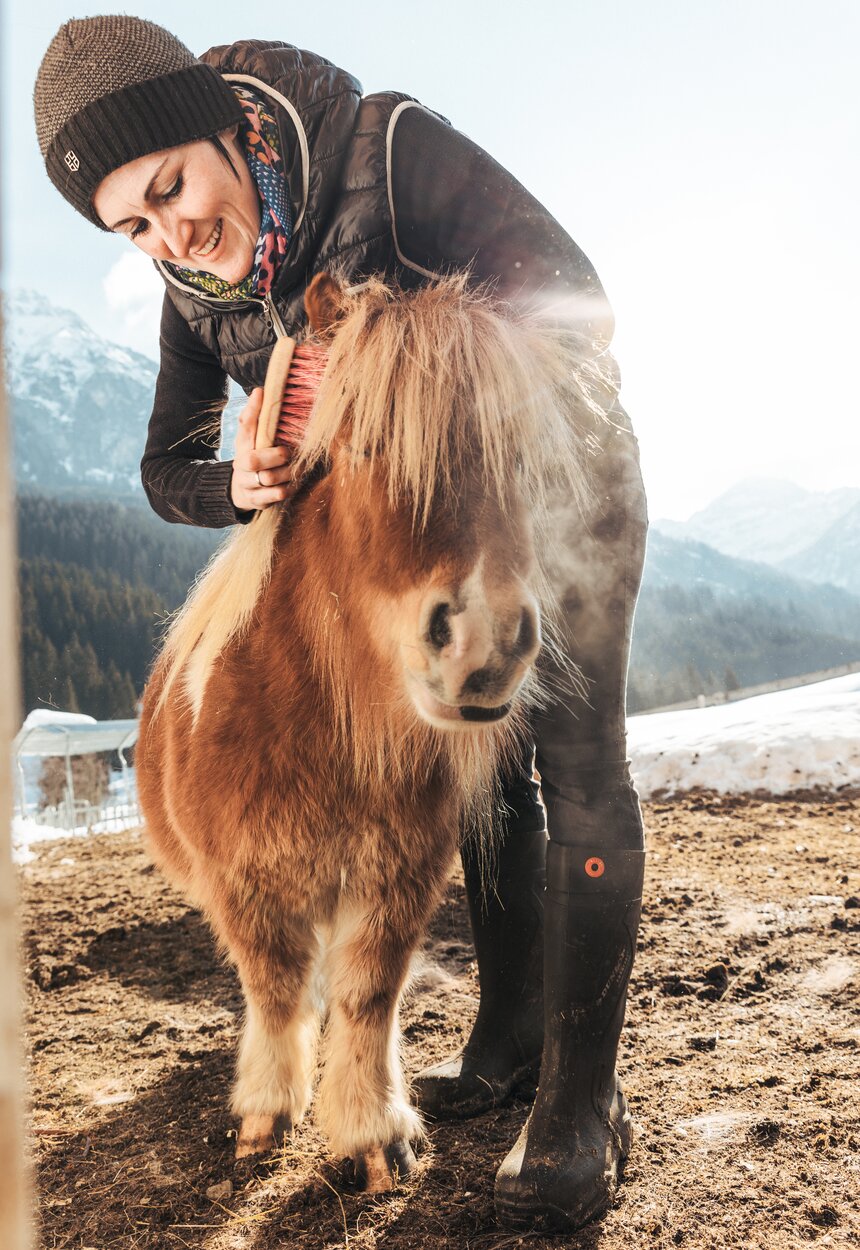 Eine Frau striegelt ein Pony | © Urlaub am Bauernhof / Punkt und Komma