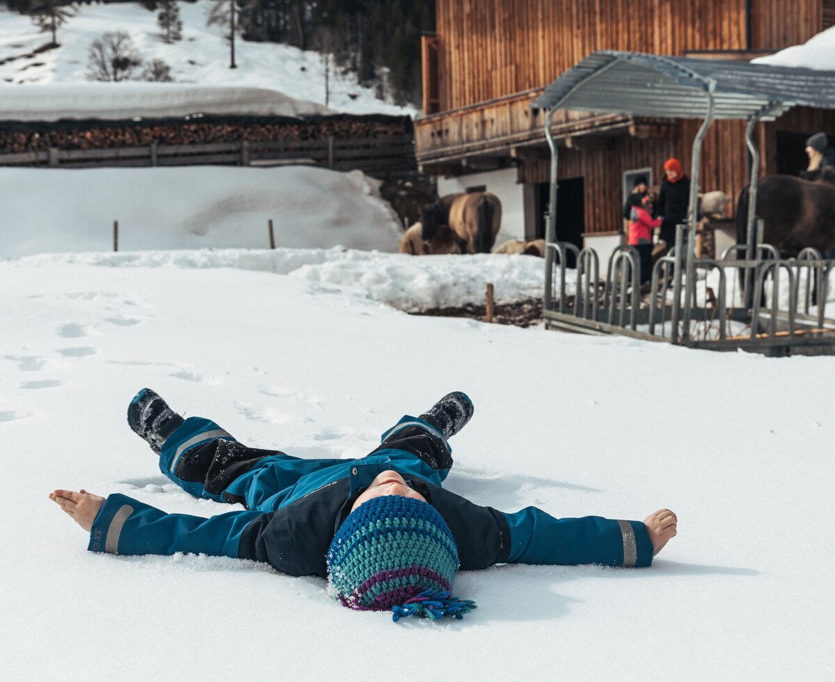 Ein kind liegt im Schnee und macht einen Schneeengel | © Urlaub am Bauernhof / Punkt und Komma