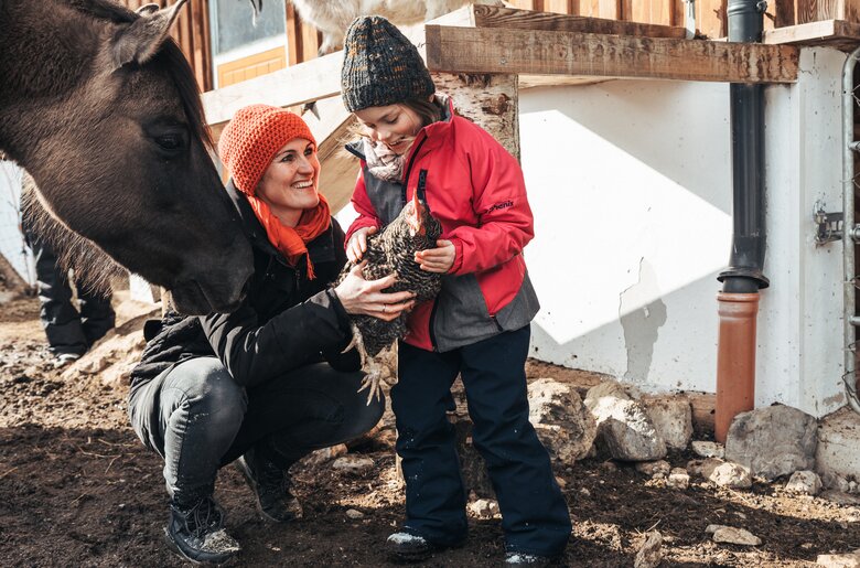 Ein Kind hält ein Huhn im Pferdestall | © Urlaub am Bauernhof / Punkt und Komma