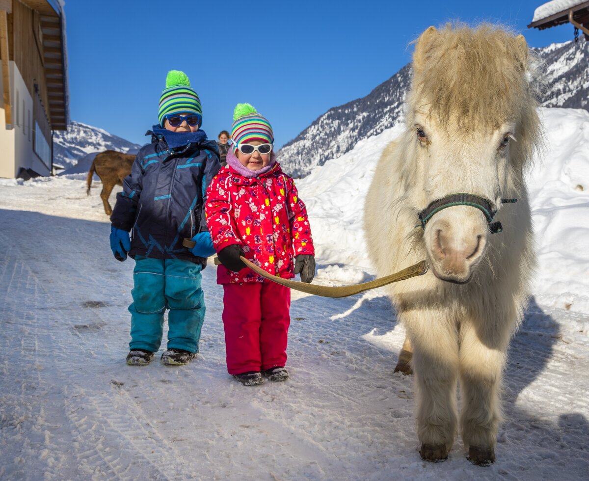 zwei Kinder stehen mit weißen Pferd in Schneelandschaft | © Urlaub am Bauernhof / Bernd Suppan