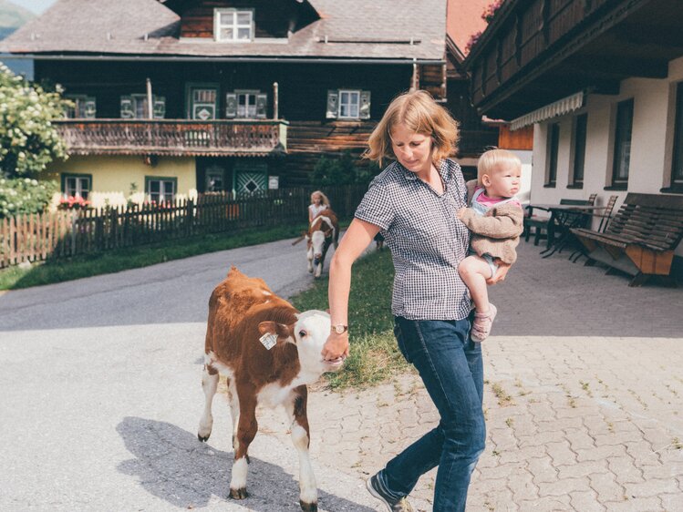 Farmer Kathrin Röck from the Grußberggut in Bad Hofgastein holds her baby on her arm and leads a calf around the farm | © Farmholidays in SalzburgerLand / Daniel Gollner