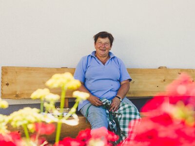 Host Karin Pöllmann from the Stallerbauer in Ried am Wolfgangsee sits on the house bench. | © Farmholidays in SalzburgerLand / Matthias Gruber