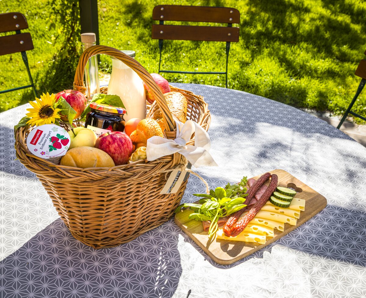 Korb mit diversen Produkten, Joghurt, Weckerl, Brötchen, Marmelade, Milch, Obst, am Tisch liegt Jausenbrett mit Wurst und Käse, Sinnhubbauer in Altenmarkt, Salzburger Land | © Urlaub am Bauernhof / Bernd Suppan