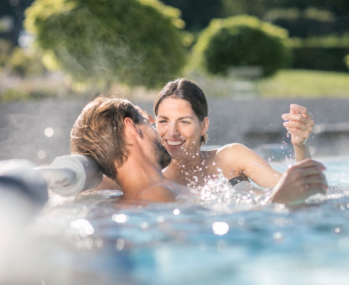 Ein Paar sitzt am Beckenrand im sprudelnden Thermalwasser, Thermen- & Vulkanland, Steiermark | © Thermen- & Vulkanland / Harald Eisenberger