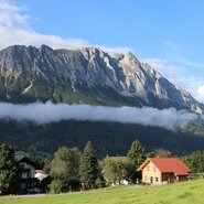 Ferienhaus am Bauernhof unter Bäumen und im Hintergrund der mächtige Grimming | © UaB / Familie Royer