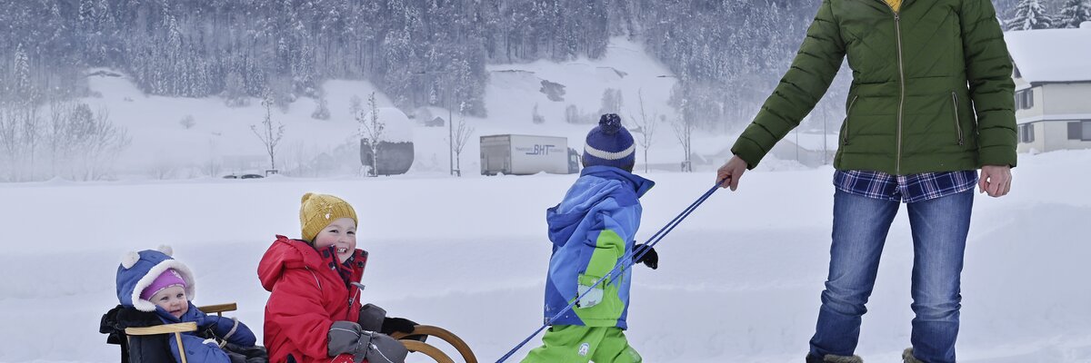 Eine Frau zieht 3 Kinder auf dem Rodel | © Urlaub am Bauernhof / Andreas Künk