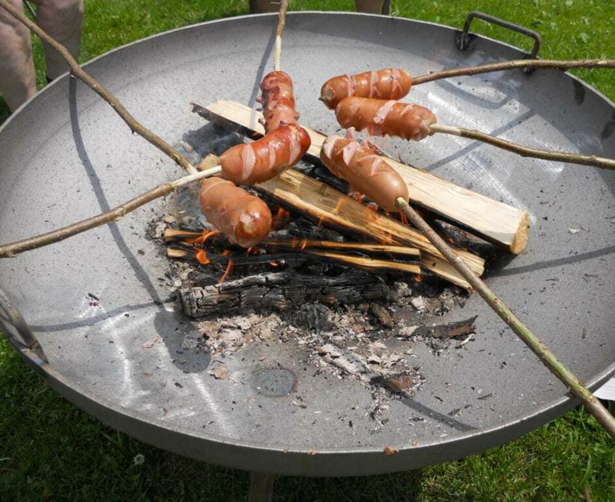 Knackwurst on grill sticks over an open fire of a grill tray.