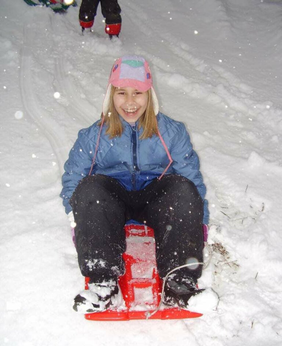 Girl riding a red skibob in the snow.